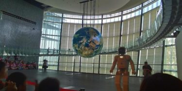 大きな地球儀の前に立ち観客を見るロボット